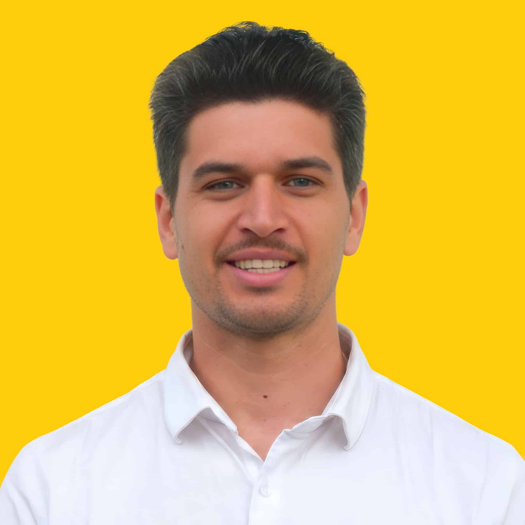 Man smiling, wearing a white shirt, against a bright yellow background.